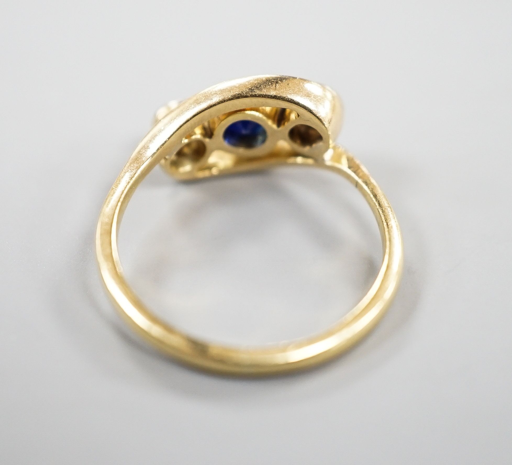 A modern 18ct gold, single stone diamond and two sapphire set crossover ring, size K, gross 3.2 grams.